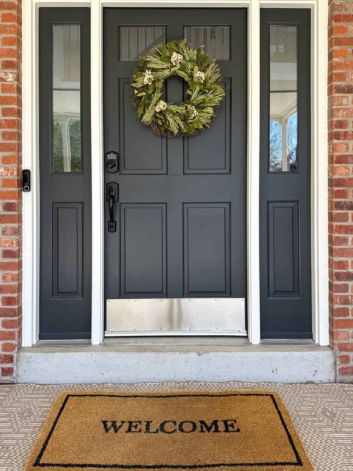 the green florals and wheat grass on this outdoor summer wreath really pop on top of the dark blue door 